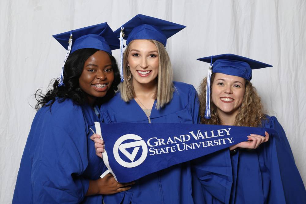 Three friends with their caps and gowns pose together at GradFest